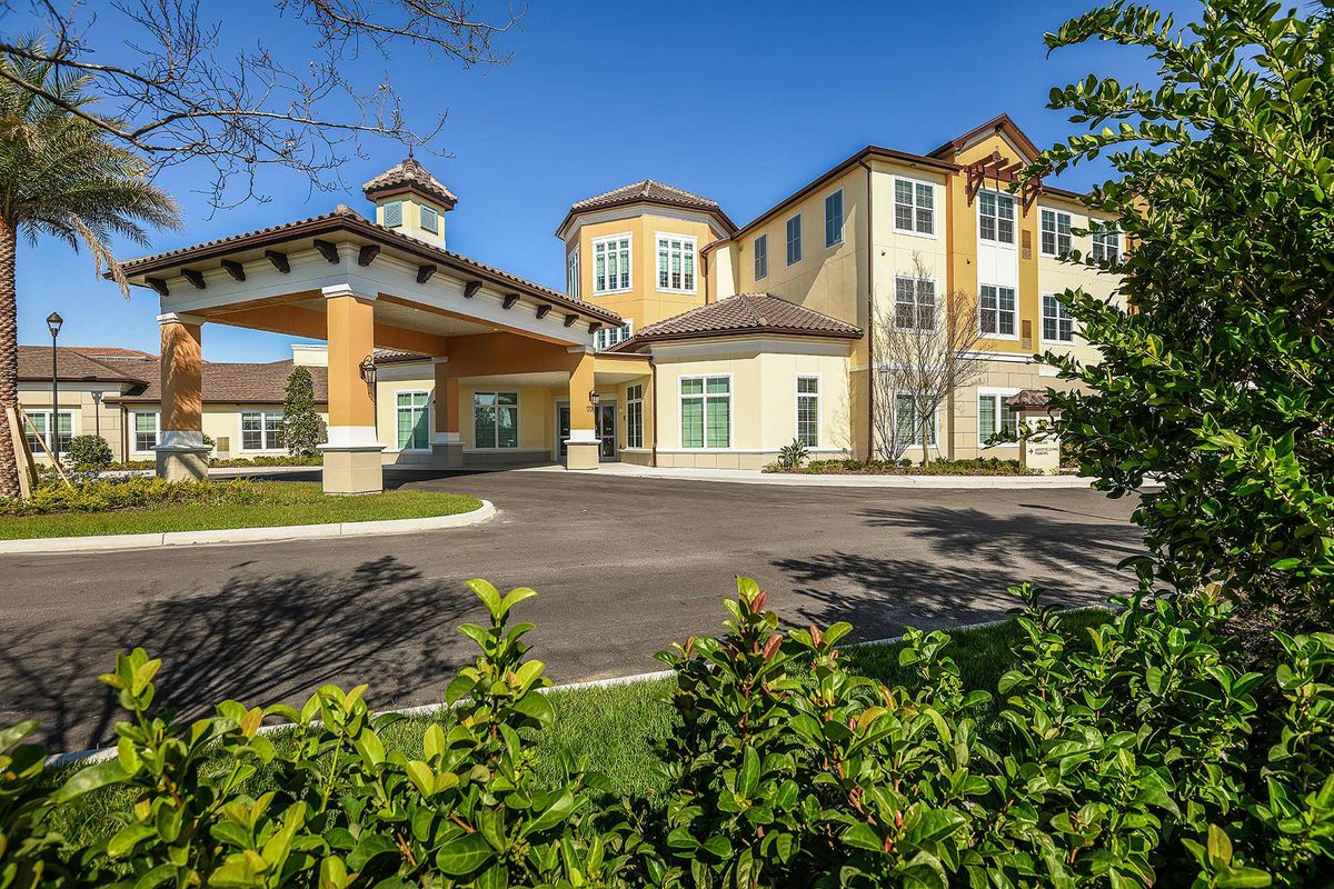 A modern residential building with a covered entrance and well-maintained landscaping on a sunny day.