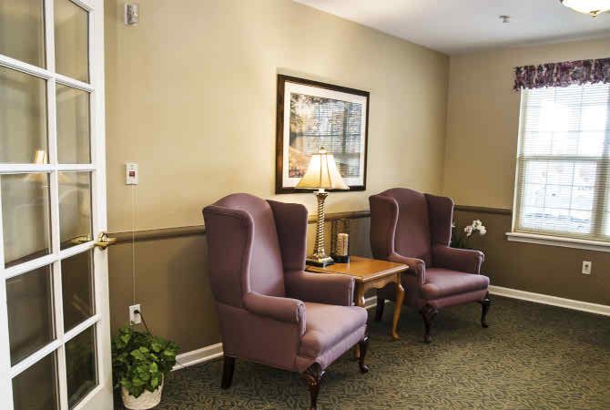 A cozy lounge area featuring two wingback chairs, a wooden table with a lamp, and wall art.