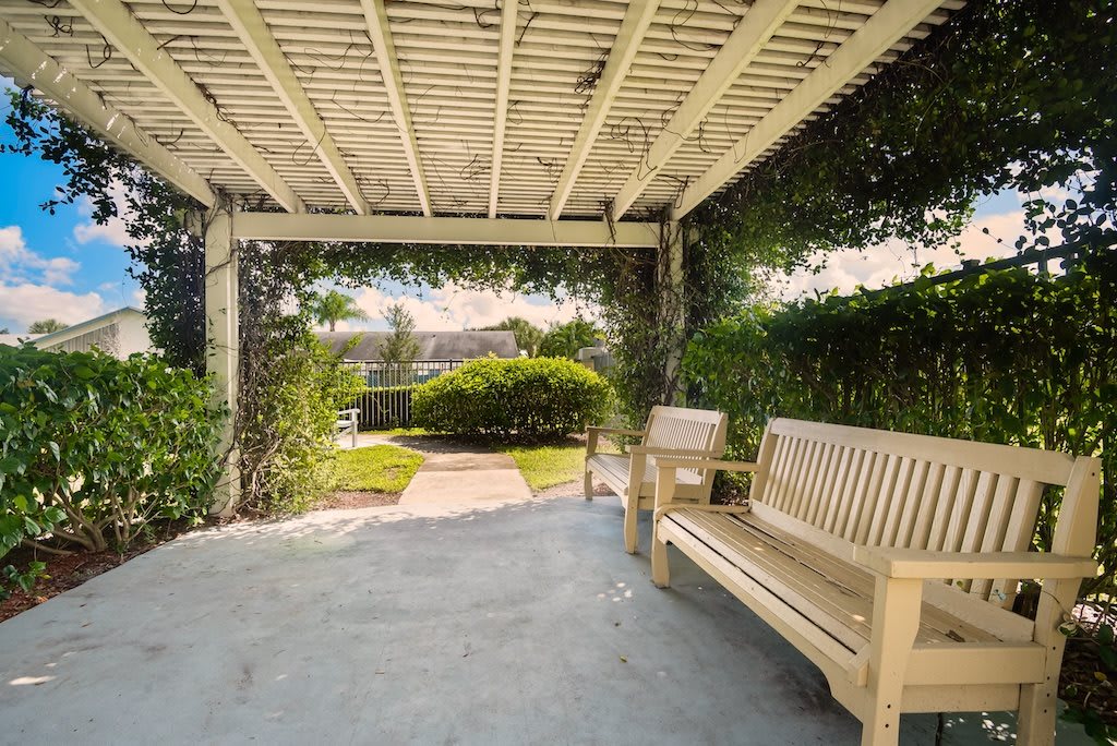 A tranquil pergola with benches in a lush garden setting.