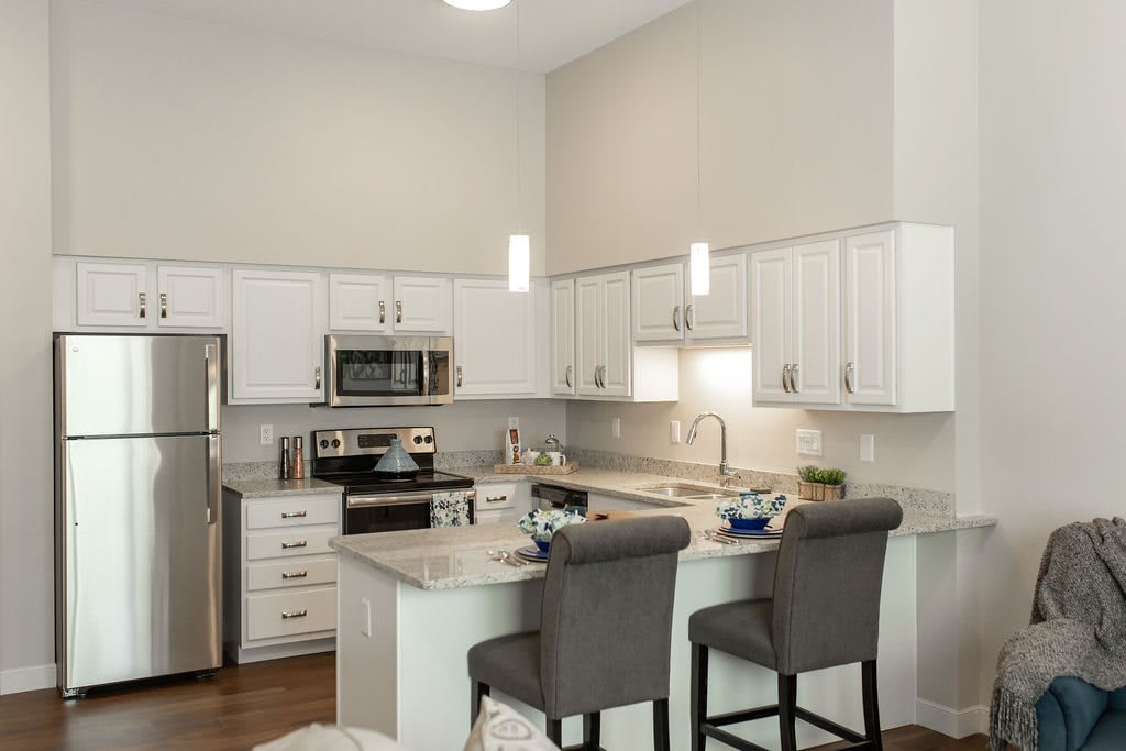 A modern kitchen with white cabinets, stainless steel appliances, and bar stools at the countertop.