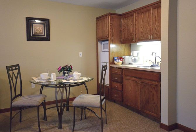 A cozy kitchen setup with a small dining area, featuring wooden cabinets and a glass-top table with chairs.