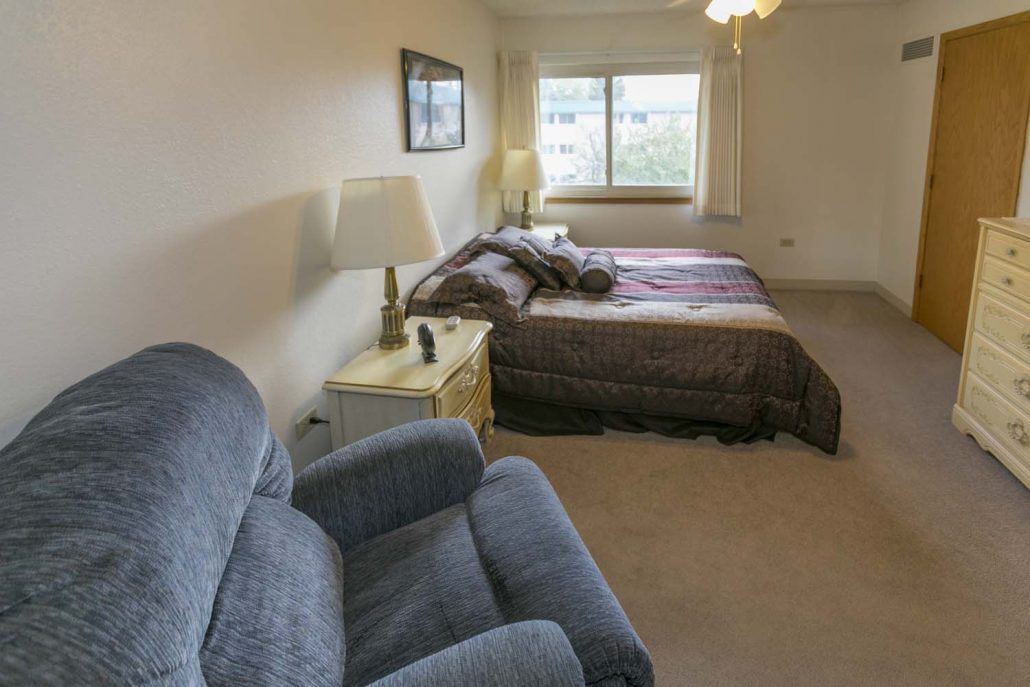 A cozy bedroom with a bed, lamp, and armchair by the window.