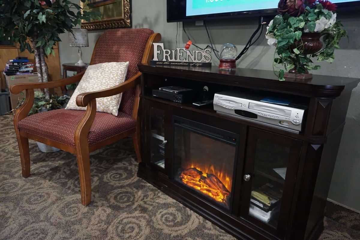 A cozy living room with an upholstered chair, electric fireplace, and a television.