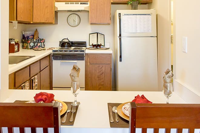 A cozy kitchen with a dining area set for two, featuring a stove and refrigerator.