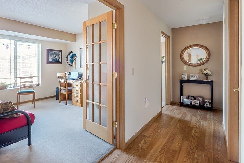 A cozy home interior featuring a hallway with wooden flooring leading to an office space through a French door.