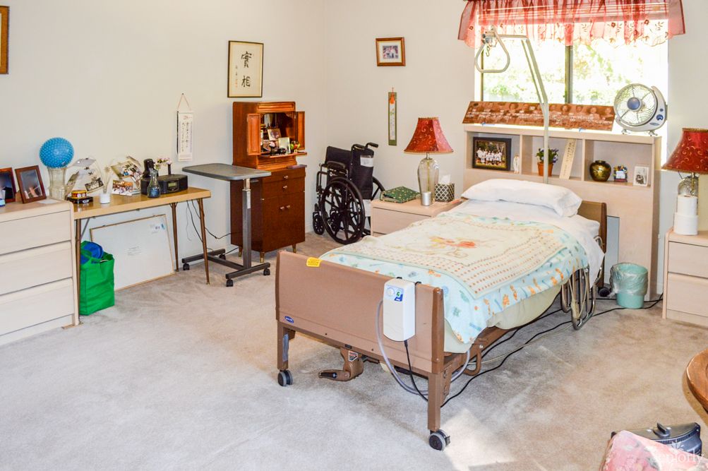 A care facility room with a hospital bed and wheelchair.