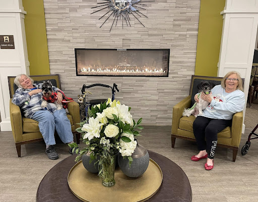 A cozy lounge area featuring a fireplace and a floral arrangement, where two seniors enjoy their time together.