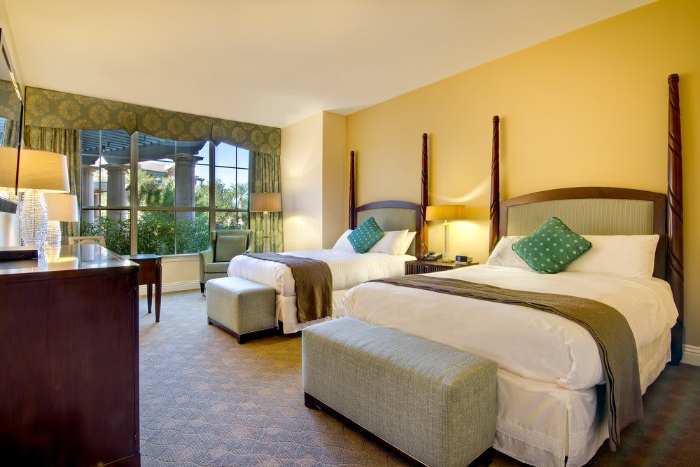 A spacious hotel room with two double beds, modern decor, and a large window offering a scenic view.