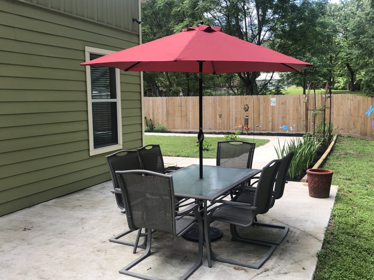 A backyard patio setup with a table, chairs, and a red umbrella.