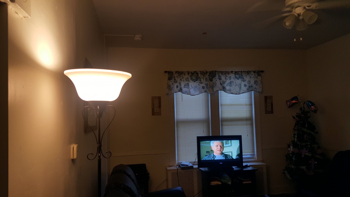 A cozy living room with a lit lamp, television, and curtained windows.