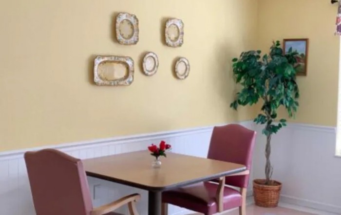 A cozy dining area with a table, two chairs, decorative wall frames, and a potted plant.