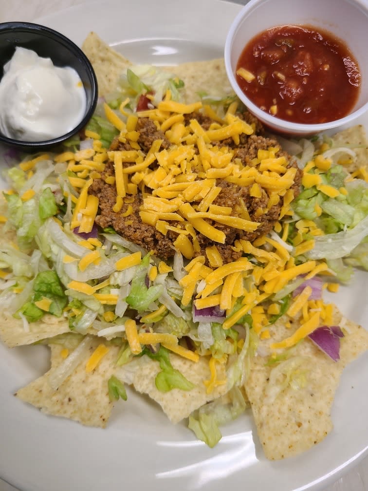 A plate of nachos topped with beef, shredded cheese, lettuce, and served with sides of sour cream and salsa.