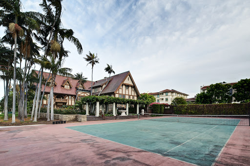 A beautiful mansion with a tennis court surrounded by palm trees.