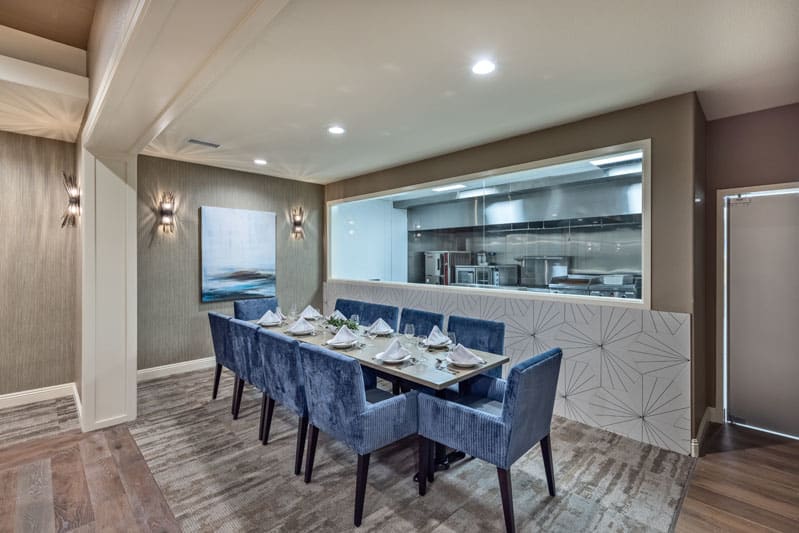 A modern dining room with a large table set for eight, adjacent to an open kitchen area.
