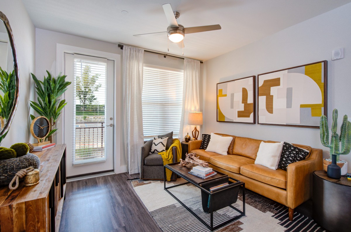 A modern living room with a leather sofa, abstract artwork on the wall, and ample natural light coming through glass doors.