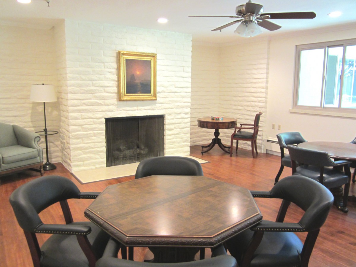 A cozy room featuring a fireplace, a wooden table with chairs, and a ceiling fan.