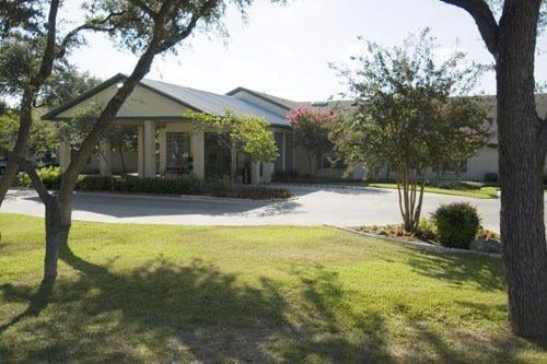 A residential house with a driveway, surrounded by trees and a well-maintained lawn on a sunny day.