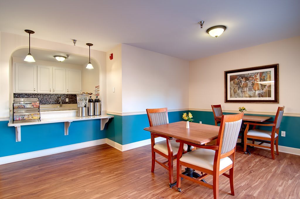 A modern dining area with wooden flooring, featuring tables and chairs, an open kitchen counter, and decorative lighting.