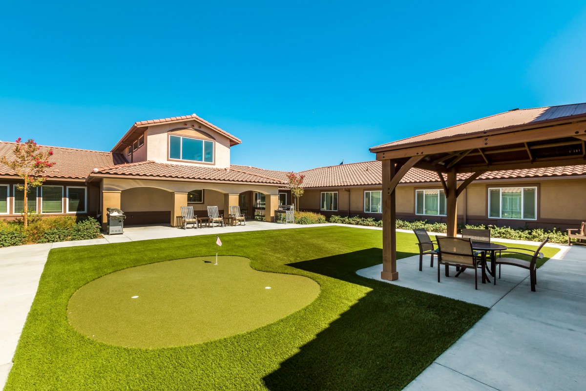 A residential backyard featuring a small putting green and patio gazebo under a clear blue sky.