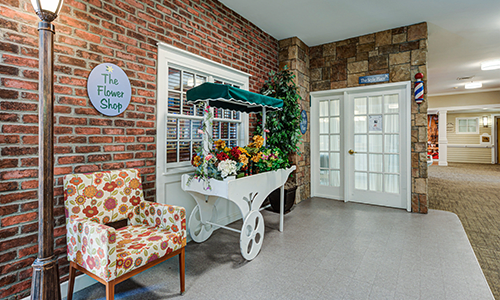 A cozy interior featuring a decorative flower cart and a floral-patterned chair against a brick wall.
