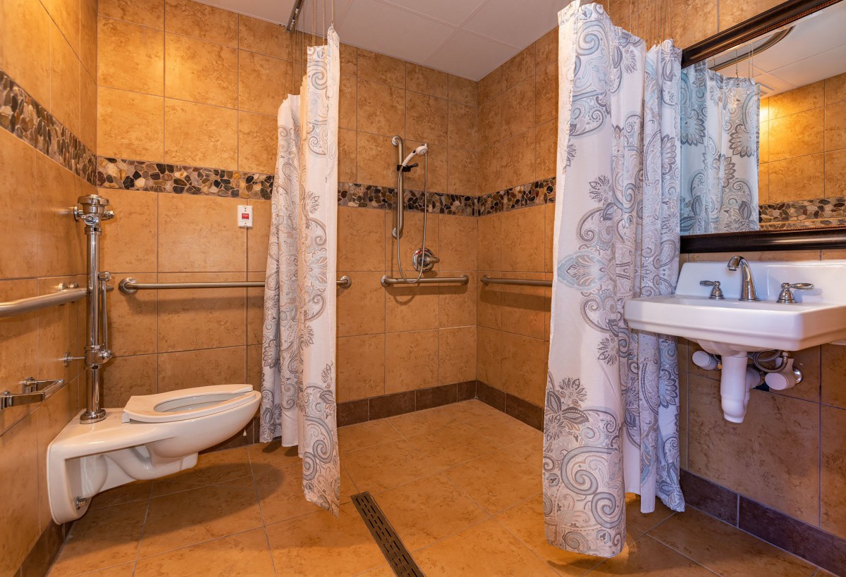 An accessible bathroom with a shower area equipped with curtains, a wall-mounted toilet, and a sink.