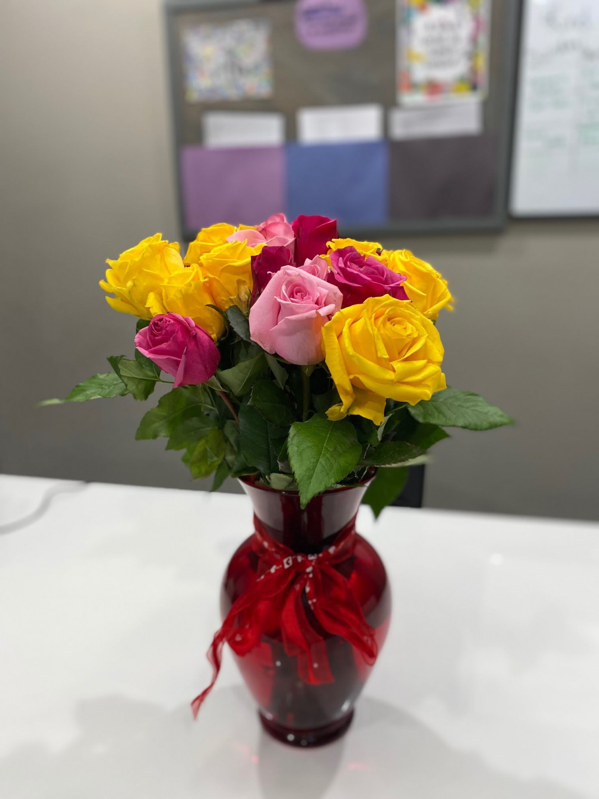 A colorful bouquet of yellow and pink roses arranged in a red vase with a ribbon.