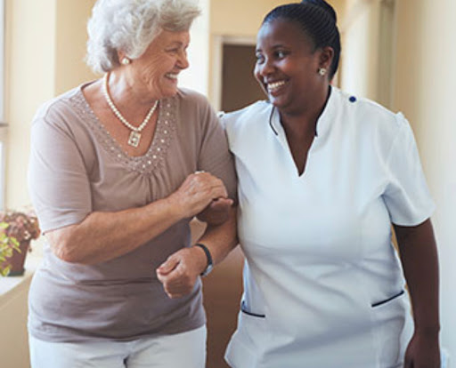 A caregiver and an elderly woman enjoy a warm moment while walking together.