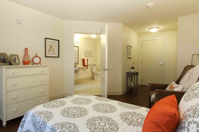 A cozy bedroom interior with a bed, dresser, and an open doorway to a bathroom.