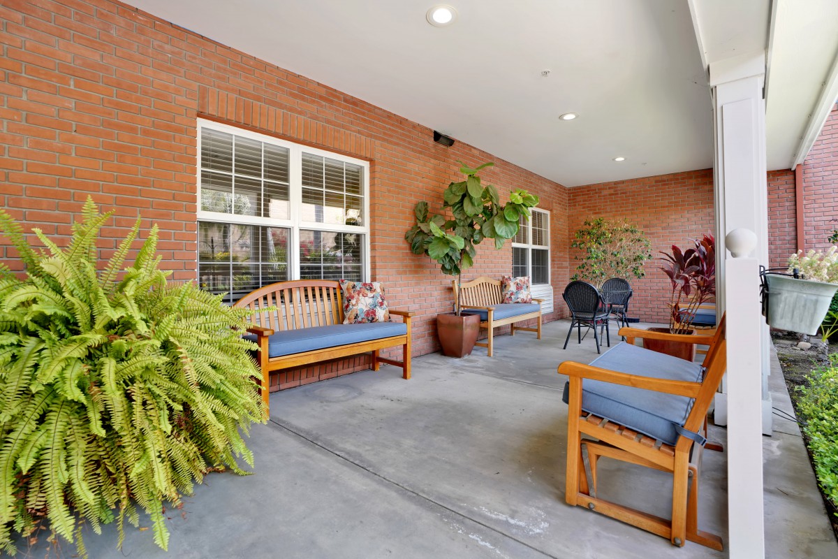 A cozy patio with wooden benches and potted plants against a brick wall.