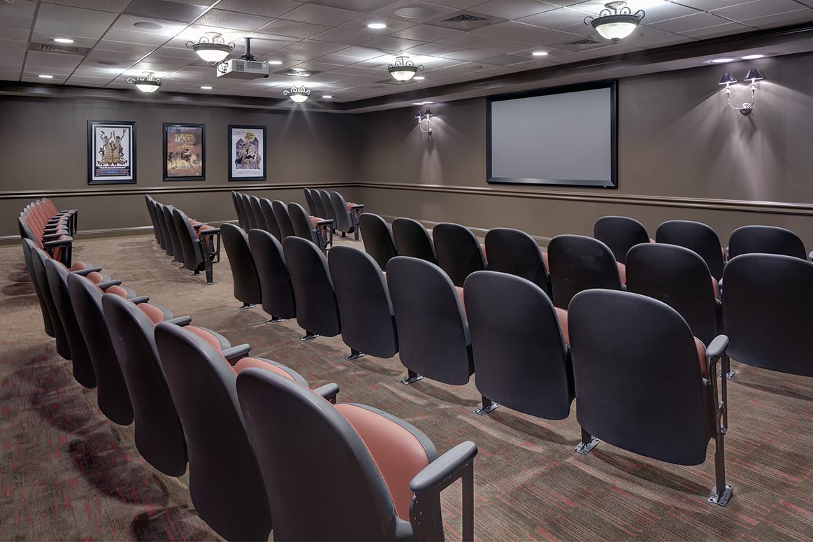 An empty theater room with rows of seats facing a large screen.