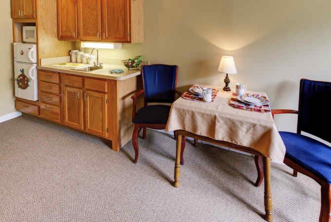 A small kitchen and dining area with a table, lamp, and cabinets.
