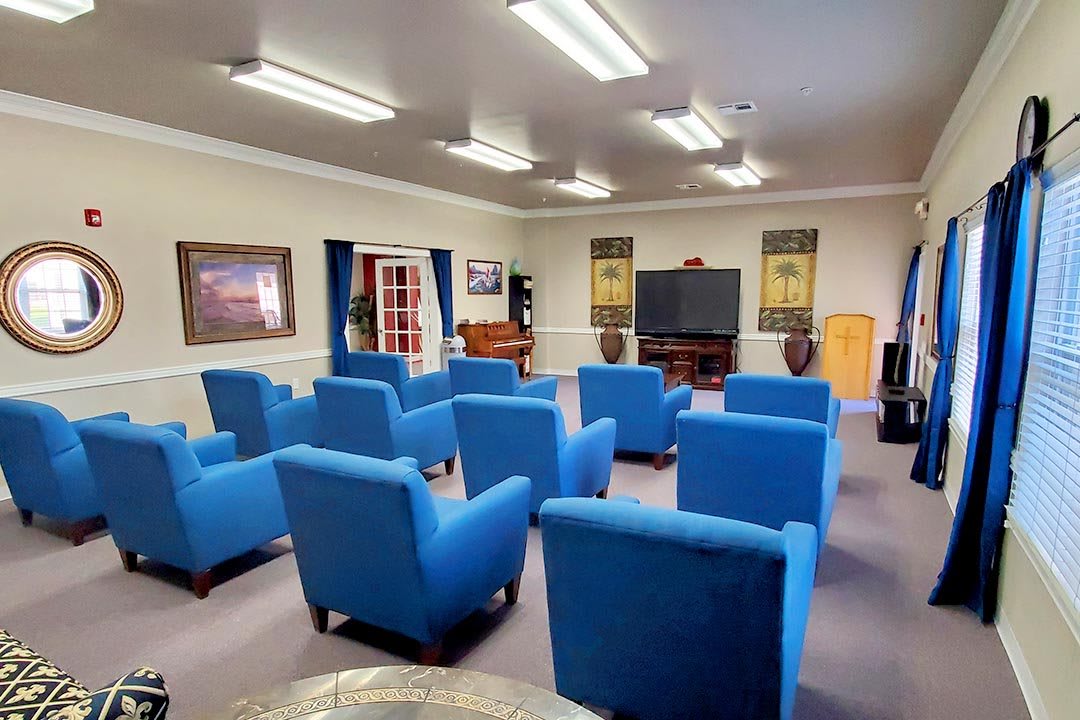 A brightly lit meeting room with rows of blue chairs facing a television and lectern.