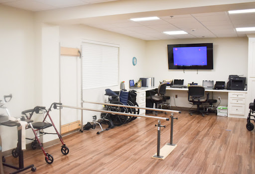 A rehabilitation therapy room equipped with parallel bars, a walker, and workstations for patients.