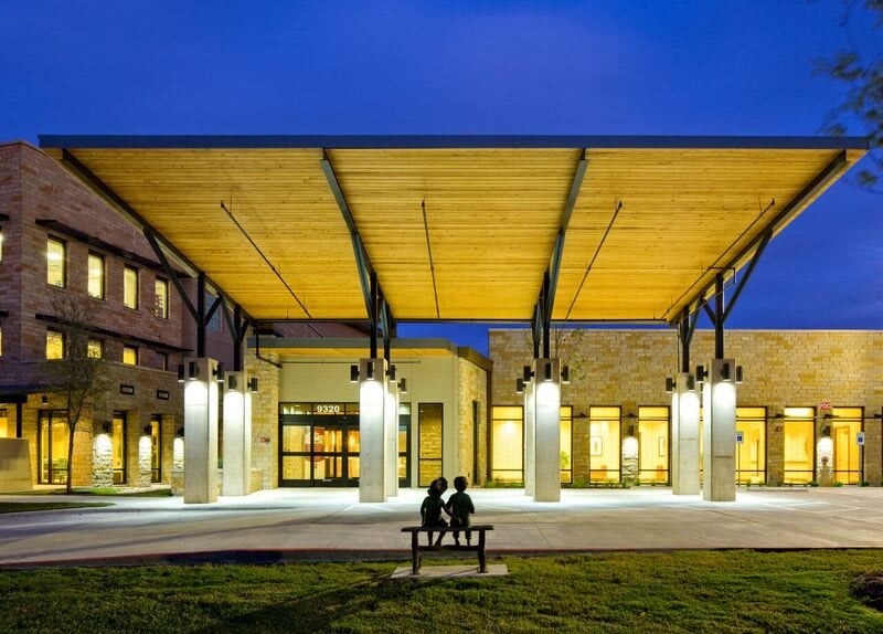 A modern building with a wooden canopy and outdoor seating, illuminated at night.