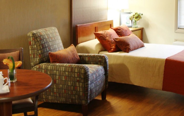 A cozy hotel room featuring an armchair, a bed with multiple pillows, and soft lighting.