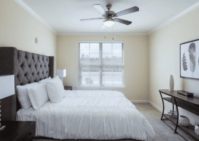 A cozy bedroom with a neatly made bed, a ceiling fan, and natural light from the window.