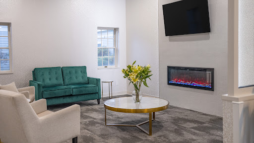 A modern living room featuring a green couch, elegant coffee table, and an electric fireplace.