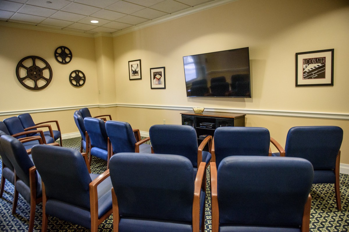 A small conference room with rows of chairs facing a large television on the wall.