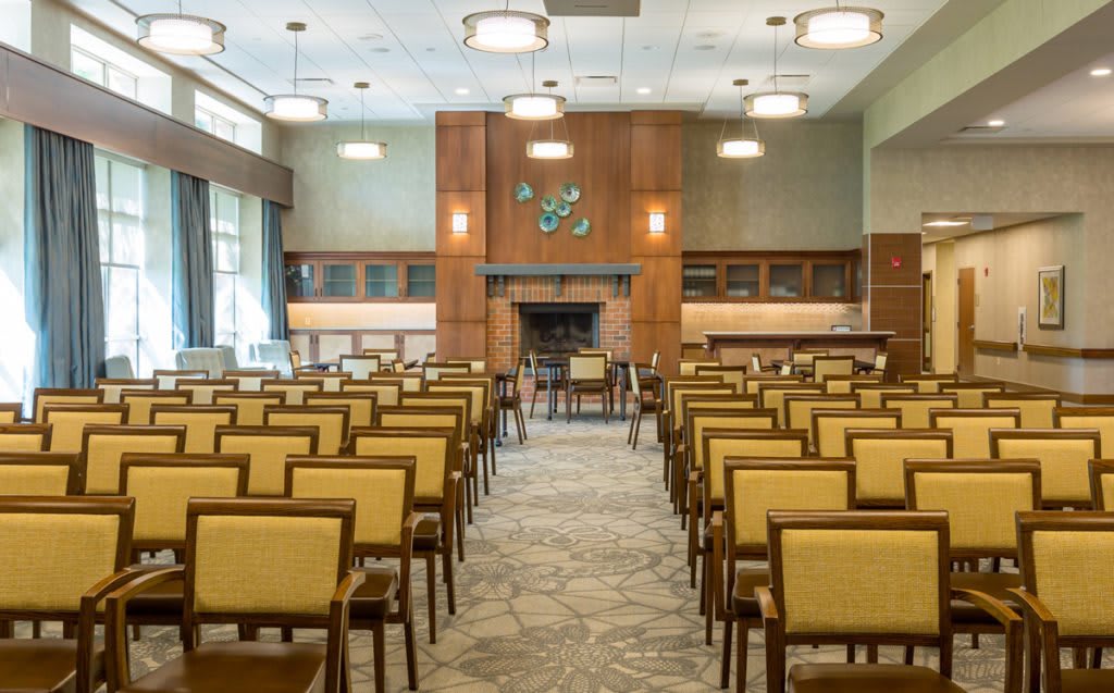 A modern conference room with rows of chairs facing towards a central wooden feature wall and lighting fixtures hanging from the ceiling.