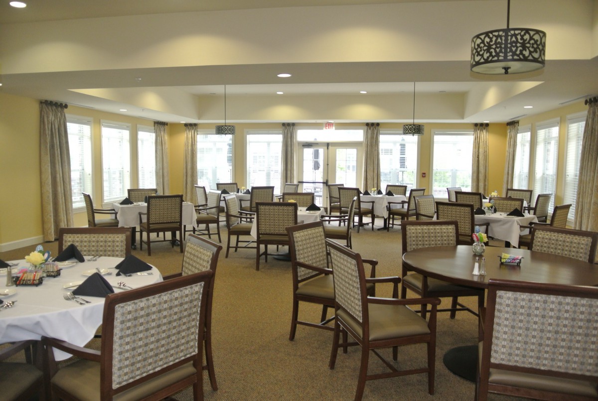 An elegantly arranged dining room with multiple tables and chairs, featuring large windows that allow natural light to flood in.