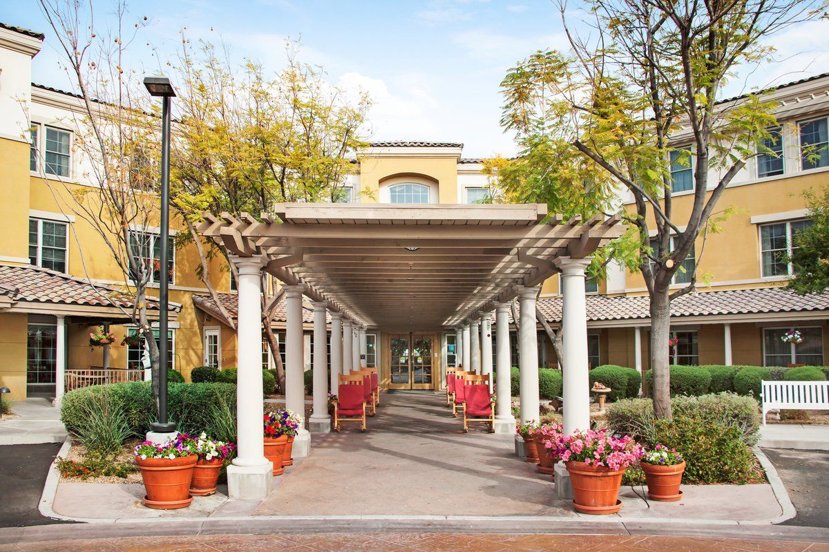 A scenic walkway with a pergola, flanked by potted plants and benches, leading to a building.