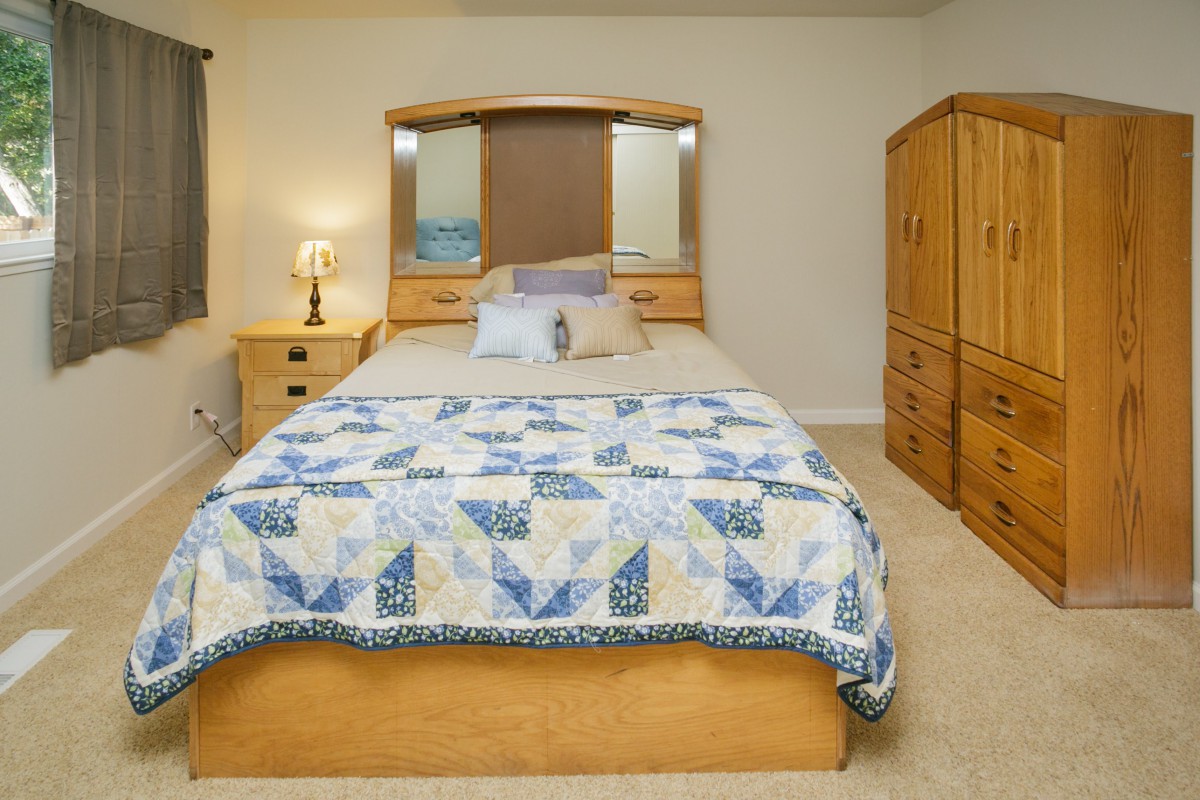 A cozy bedroom with a neatly made bed featuring a blue and white quilt, surrounded by wooden furniture and a glowing lamp on the nightstand.