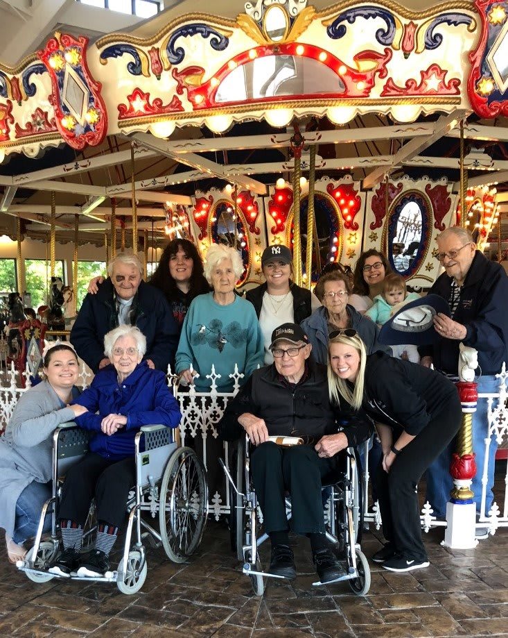 A group of elderly individuals enjoying a day out at the amusement park, gathered around a carousel.