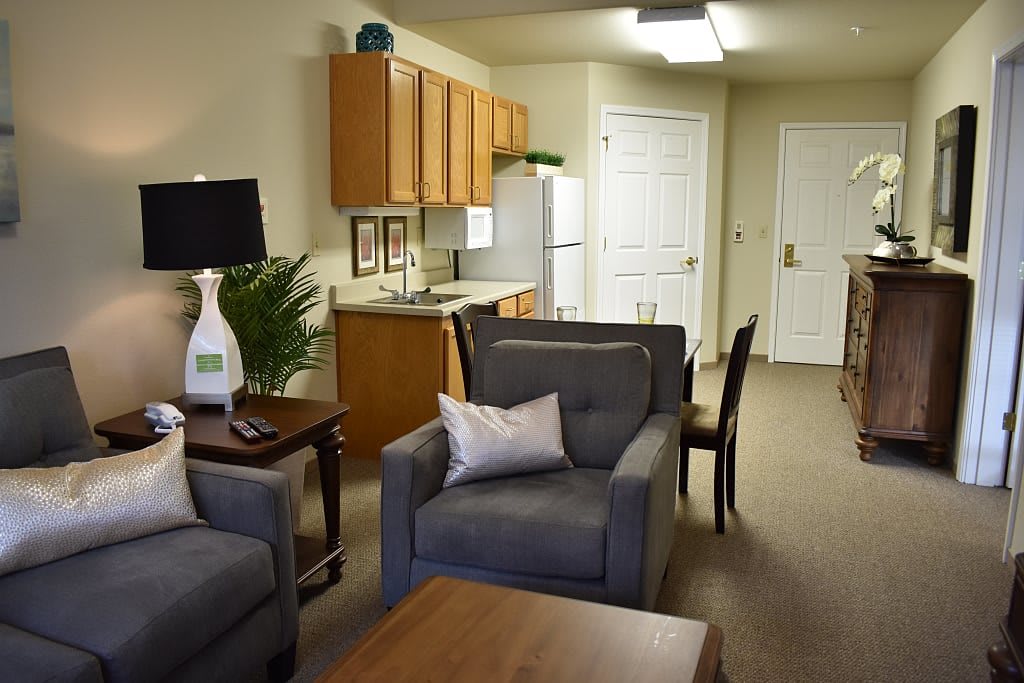 A cozy apartment living area featuring a kitchen with wooden cabinets, a comfortable sofa, and a stylish lamp on a side table.