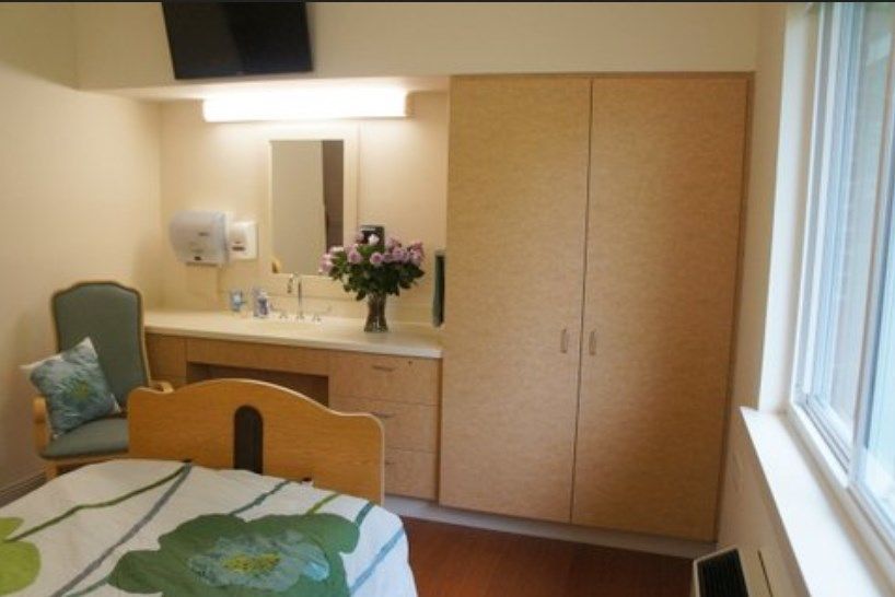 A small hospital room with a bed, wardrobe, mirror, and a vase of flowers.