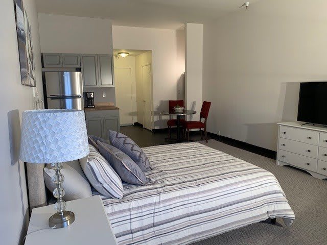 A spacious studio apartment featuring a bed, kitchen area, and dining table.
