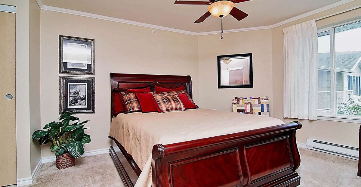 A cozy bedroom with a dark wooden bed, neutral bedding, and a ceiling fan.
