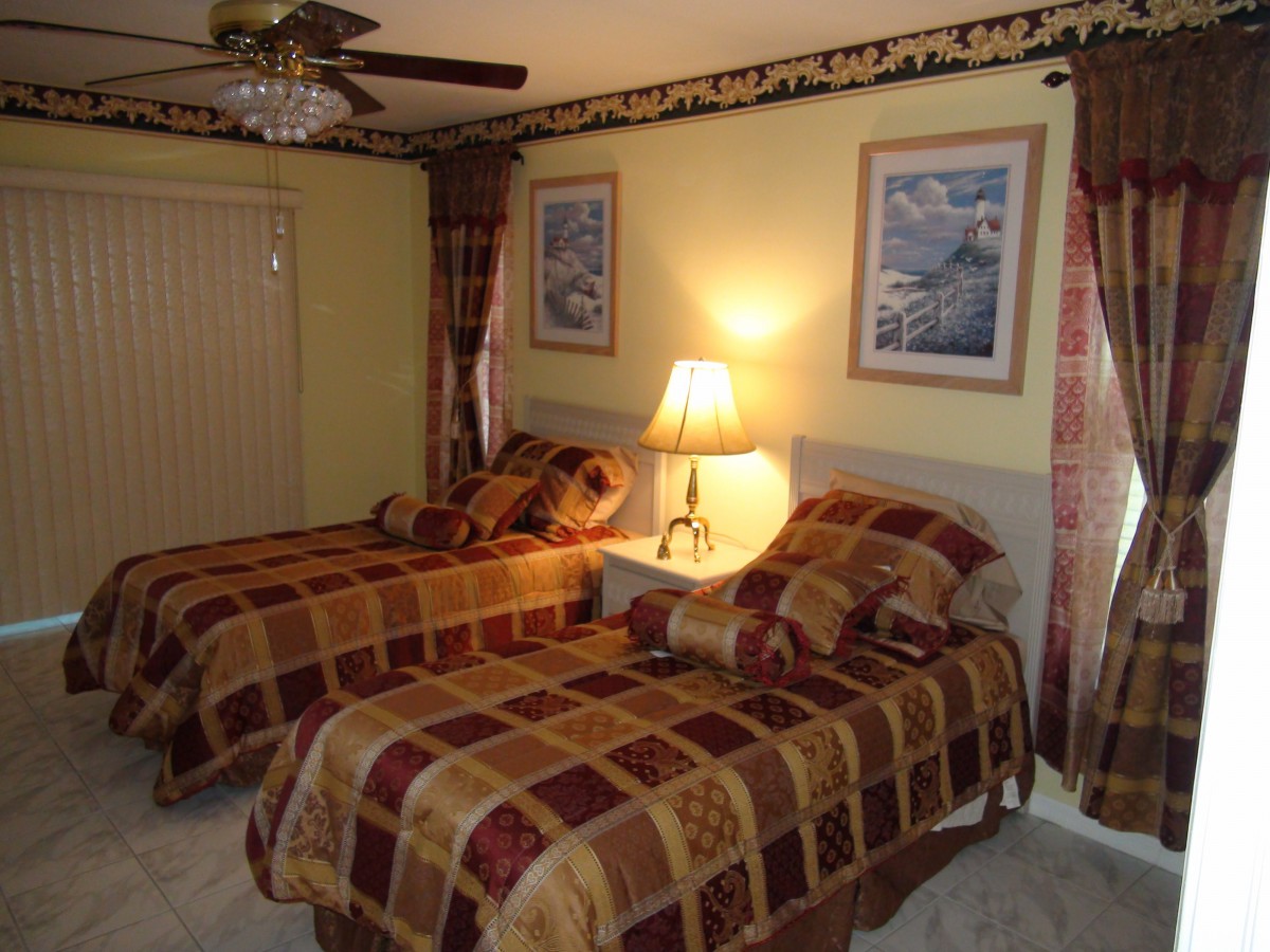 A cozy bedroom featuring two twin beds with matching bedspreads, a lamp on a nightstand, and framed artwork on the walls.