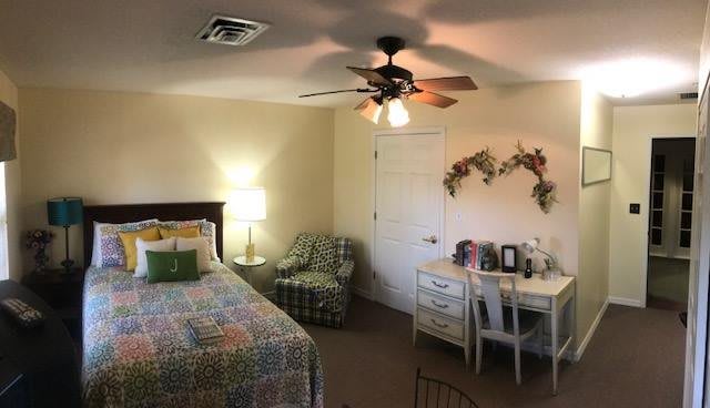 A cozy bedroom with a bed, lamp, and desk, featuring homey decorations and a ceiling fan.