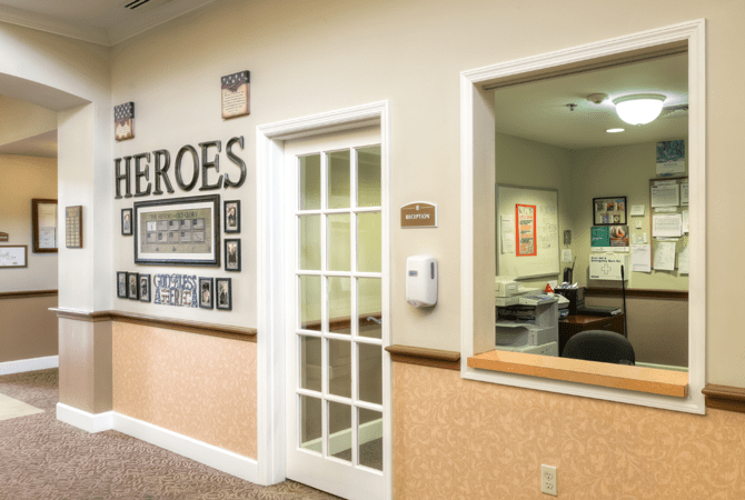 A hallway with a 'Heroes' wall display of photographs, next to an office door and reception window.